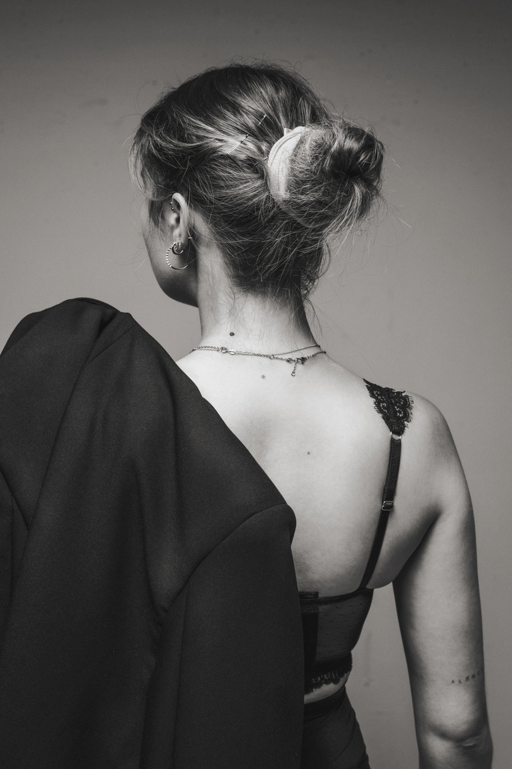 Schwarzweißbild einer Frau, die mit dem Rücken zur Kamera steht. Sie schaut nach links, hat einen Blazer über die Schulter gelegt und trägt ein Bustier.
